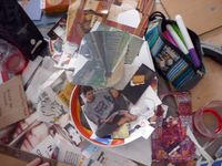 Photo en vue du dessus d'un bazar de papiers découpés de magazines ou journaux, tubes de colle, feutres dans une trousse ouverte, règle etc.